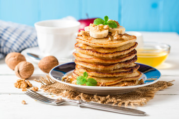 Pancakes with banana, honey, walnuts and mint on plate.