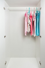 Clothes hanging on rail in white wardrobe. Men's and women's summer clothes, pastel colors