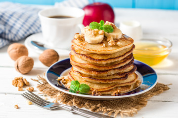 Pancakes with banana, honey, walnuts and mint on plate.