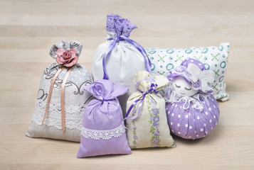 Bunch of different scented sachets for decoration on wooden board. Many fragrant pouches on table. Aromatic potpourri set. Bags filled with lavender. Decorative interior design items on table.