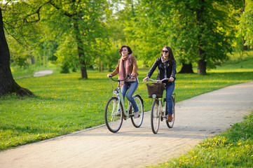 Two young attractive women ride bikes in the spring park.