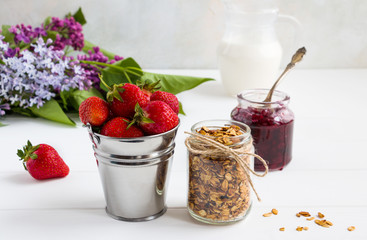 Ingredients for healthy breakfast, fresh strawberry, granola, jam and milk on the white wooden table.