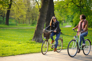 Two young women ride bikes in the spring park.