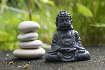 Harmony and balance, simple pebbles tower in the grass, simplicity, four stones and dark grey Buddha statuette