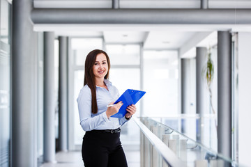 Beautiful business woman standing and holding paper board in modern business interior