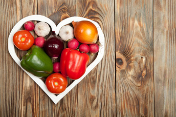 Vegetables. Peppers, tomatoes, garlic, onions, and radishes in the heart on rustic background