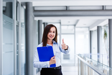 Business woman standing in modern interior and showin thumbs up