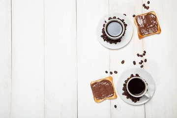 Two cups of coffee and toast with chocolate on a white wooden table