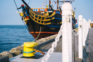 Mooring bollard on a wooden pier with docked pirate ship on the background