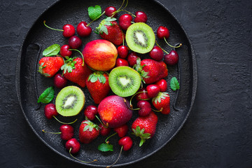 Mix of summer berries and fruits on a black plate. Top view with copy space