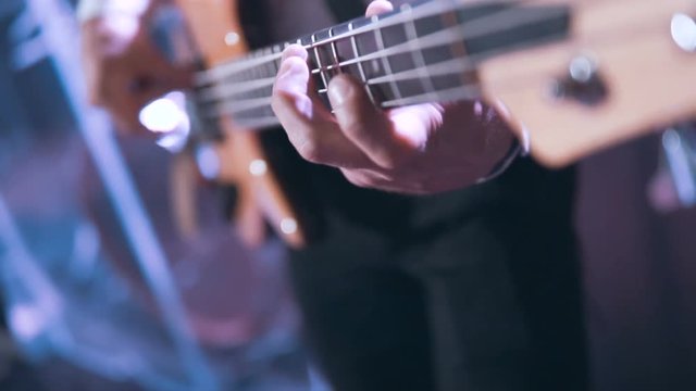 Guitarist wears white shirt playing on bass guitar on the concert stage, 100FPS slowmotion