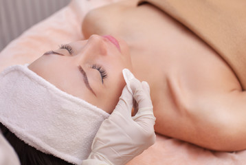 The doctor cosmetologist cleanses with a tonic the face skin of a beautiful, young woman in a...