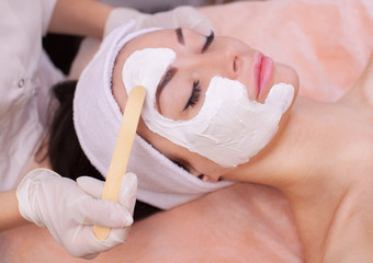 The doctor is a cosmetologist for the procedure of cleansing and moisturizing the skin, applying a mask with stick to the face of a young woman in beauty salon.Cosmetology and professional skin care.