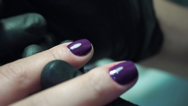 Professional manicurist, manicure work in black gloves at the beauty salon. Dark purple, beautiful pink nails, close up shot.