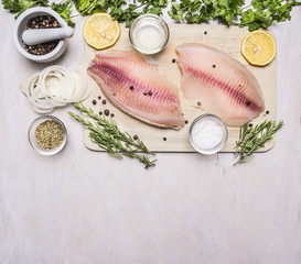 raw fillet of tilapia with spices and herbs, lemon and pepper on a cutting board on a white background rustic village top view