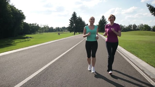 Cheerful adult fit women jogging in the park