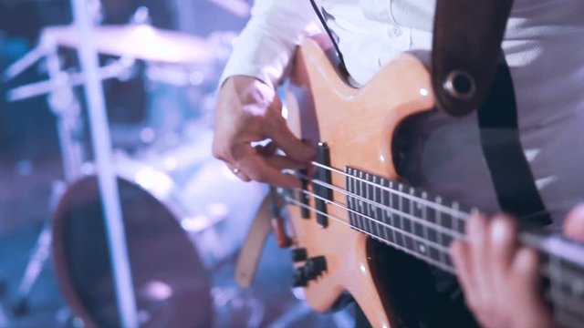 Guitarist wears white shirt playing on bass guitar on the concert stage, 100FPS slowmotion