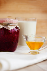 Honey, raspberry jam, milk, towel on rustic background. Candied fruits on a towel. Healthy food. Breakfast. White napkin on the table. The background. Frame
