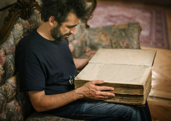 Curious man reading old book in his library at home