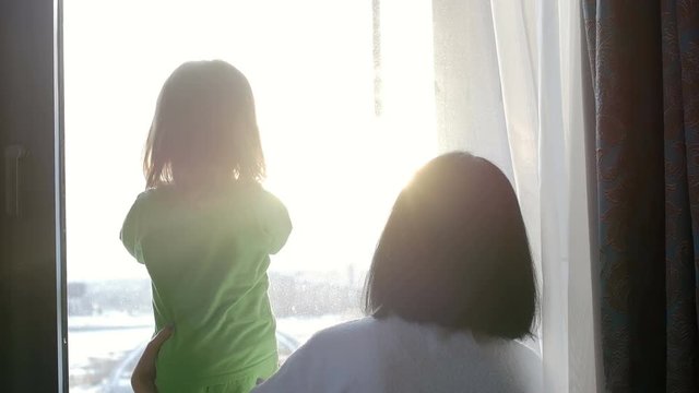 A woman and a child are looking out the window and playing with the sun. Love in the family.