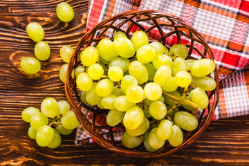 Wicker basket with grapes and napkin on wooden table