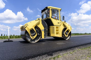 Fototapeta na wymiar Workers groomed fresh asphalt road with yellow roller