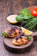 Fototapeta na wymiar Italian bruschetta with roasted vegetables, salmon, onion and herbs on a cutting board