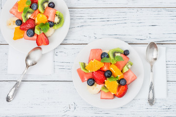 Healthy fresh fruit salad on white plate on wooden table. Top view. Delicious summer meal: strawberries, blueberries, oranges, kiwi, banana, watermelon, balm mint