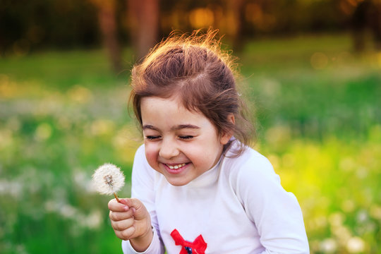 Beautiful little child with dandelion flower in sunny summer park. Happy cute kid having fun outdoors at sunset.