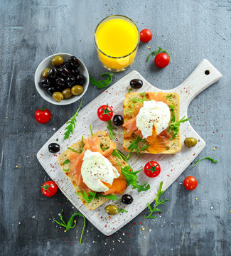 Poached egg on grilled toast with smoked salmon, rucola, olives, vegetables and orange juice. on white board. healthy breakfast