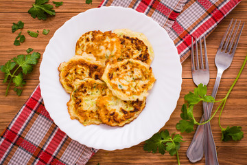Оладьи из кабачков на тарелке, зелень и вилки на деревянном столе