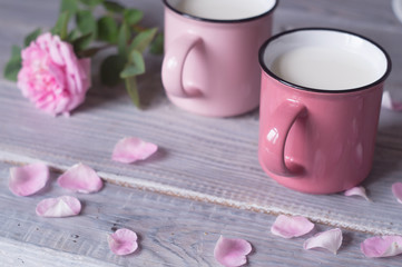 Two pink cups with milk on a white wooden table