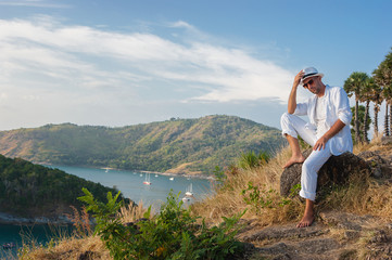 Naklejka premium young man sitting on a rock and looking at the sunset of Phuket