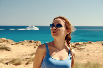 Naklejka premium Beautiful young woman in sunglasses against amazing coast. There is a boat on the sea.