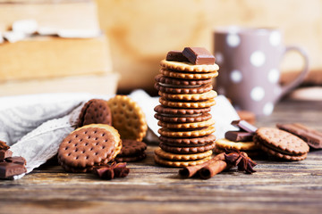 Fototapeta na wymiar Sweets and desserts, chocolate and milk biscuits sandwich, cracker with cinnamon and tea on a dark wooden rustic background 