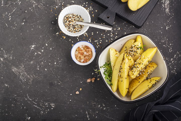 Slices of raw potatoes with sesame seeds and pink sea salt before baking in the oven on a dark background. Top view.