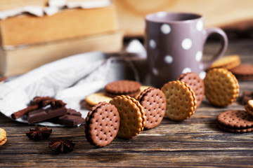 Obraz na płótnie Canvas Sweets and desserts, chocolate and milk biscuits sandwich, cracker with cinnamon and tea on a dark wooden rustic background 