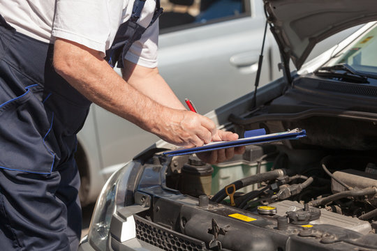 Auto mechanic checking car engine and writing on the clipboard