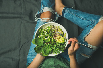 Green vegan breakfast meal in bowl with spinach, arugula, avocado, seeds and sprouts. Girl in jeans...