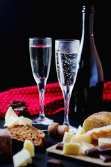 Alcoholic drinks, a holiday, white sparkling wine, glasses with champagne with freshly baked bread, mozzarella cheese and dark chocolate on a black wooden background 