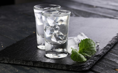 Vodka in shot glasses and ice on rustic wood background