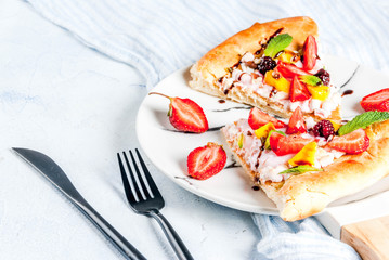 Summer snacks. Food for party. Fruit pizza with cream, currants, yogurt, strawberries, mango, peaches, bananas, blackberries, chocolate, walnuts, mint. On light blue table. Copy space