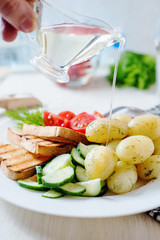Useful, hearty and delicious breakfast or dinner, boiled potato with dill, cherry tomato, cucumber, white bread toast, vegetable or olive oil and mineral sparkling water on a light wooden background
