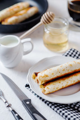 Traditional breakfast or lunch, in a hotel or restaurant, thin pancakes with cottage cheese, honey, coffee and milk on a white wooden background 