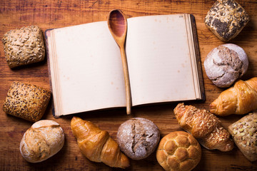 Frische, duftende Brötchen verschiedener Sorten und aufgeschlagenes leeres Backbuch mit...
