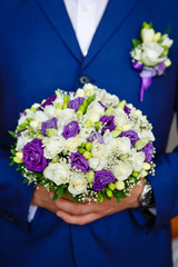 Close-up of Man the groom in the wedding blue suit with bridal bouquet with white and purple roses, flowers boutonniere on his lapel