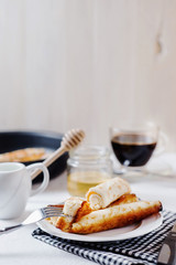 Traditional breakfast or lunch, in a hotel or restaurant, thin pancakes with cottage cheese, honey, coffee and milk on a white wooden background 