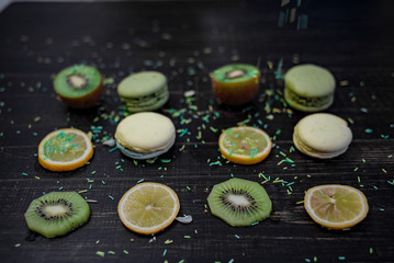 Green and white macaroons with kiwi, orange and lemon in order on a wood gark table