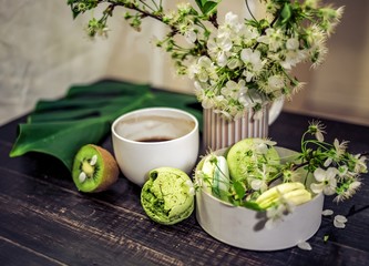 Green macarons on a wood table for coffee or a tea with the blossom flowers on background