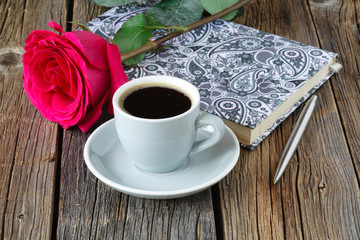 book with beautiful roses and cup of coffee on wooden table close up